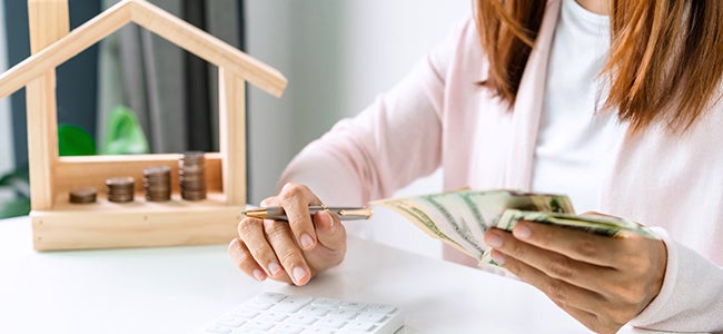Person holding money in front of a small wooden home