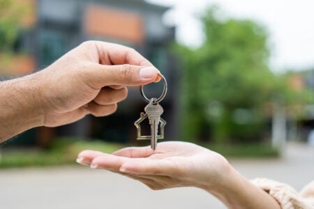 hands exchanging house key in front of new house